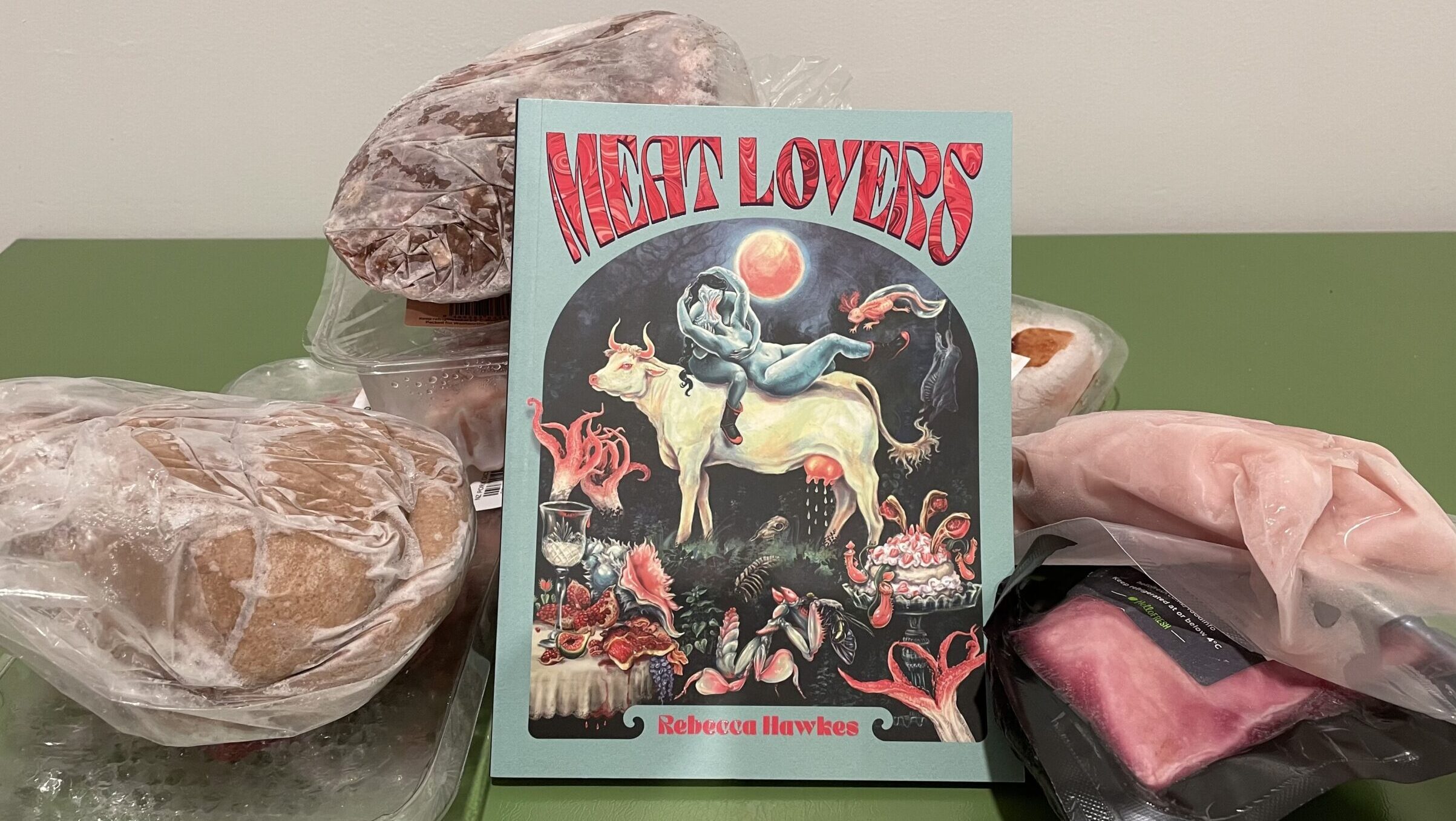 The book "Meat Lovers" by Rebecca Hawkes is propped up against a pile of frozen meat.