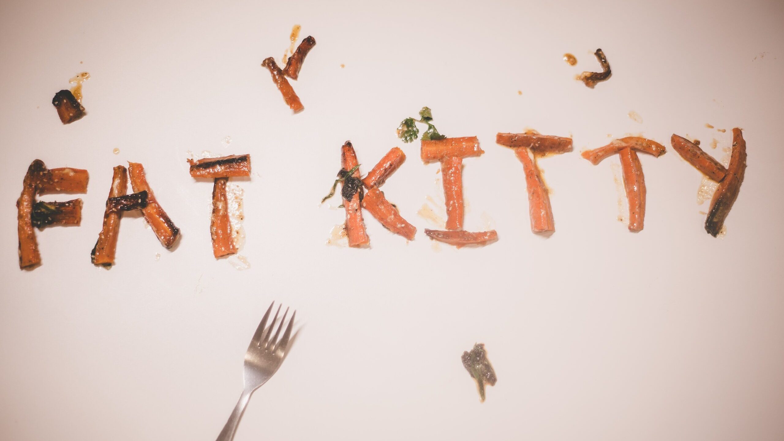 The words "Fat Kitty" are spelled out in carrots across a table.