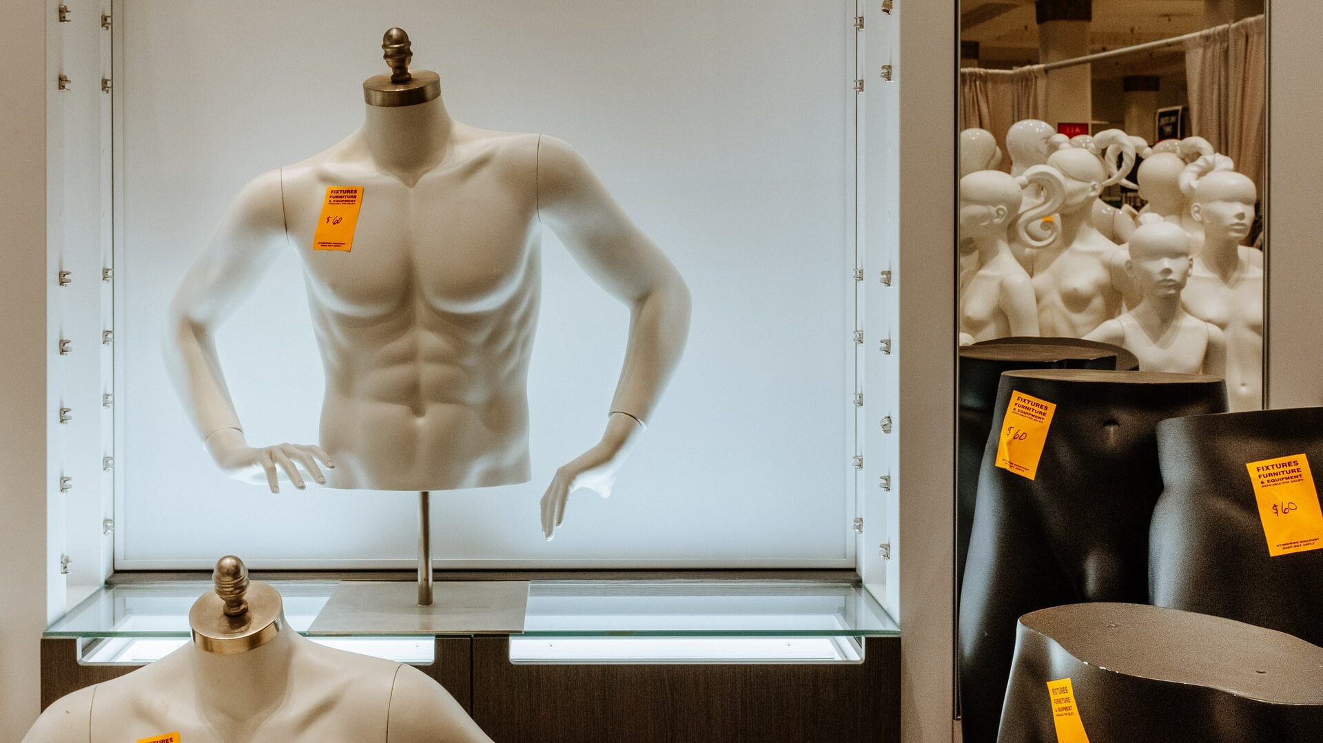 A muscular mannequin torso with a price tag on it. Several femme mannequins are piled together in the background.