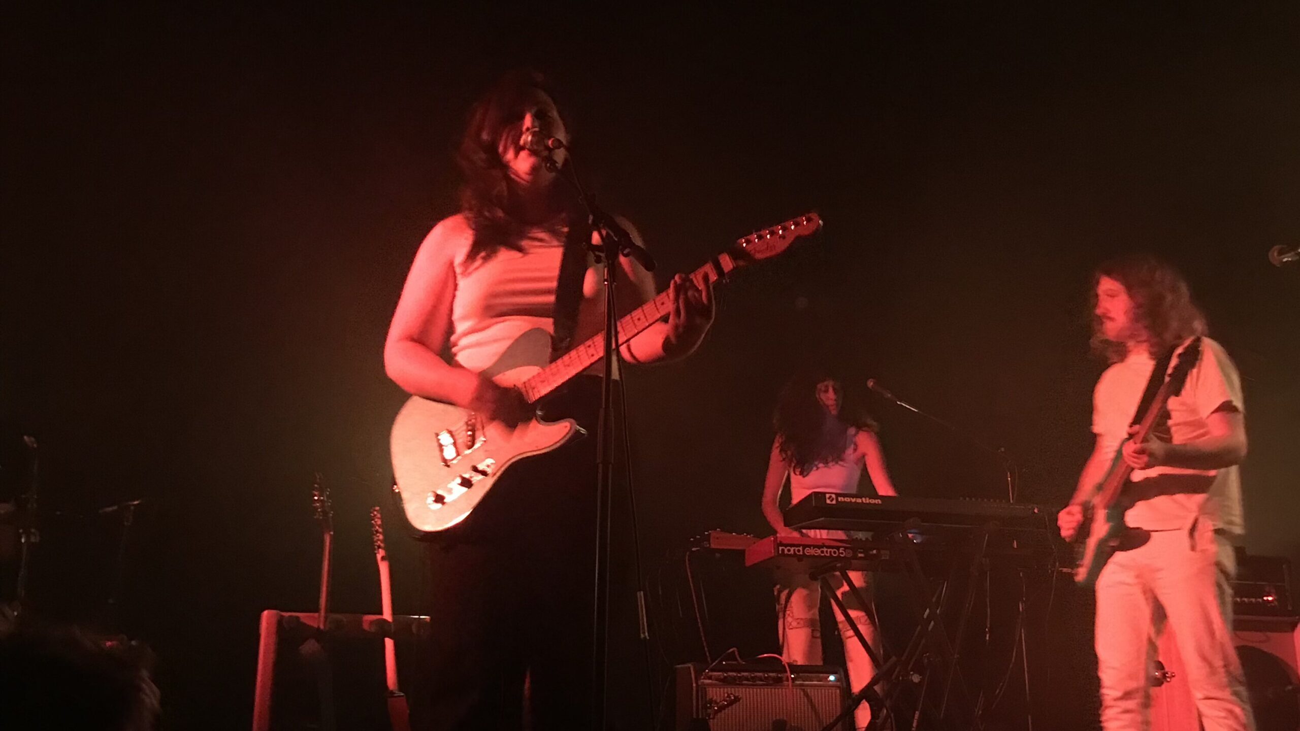 Lucy Dacus with a guitar singing into a microphone on stage.