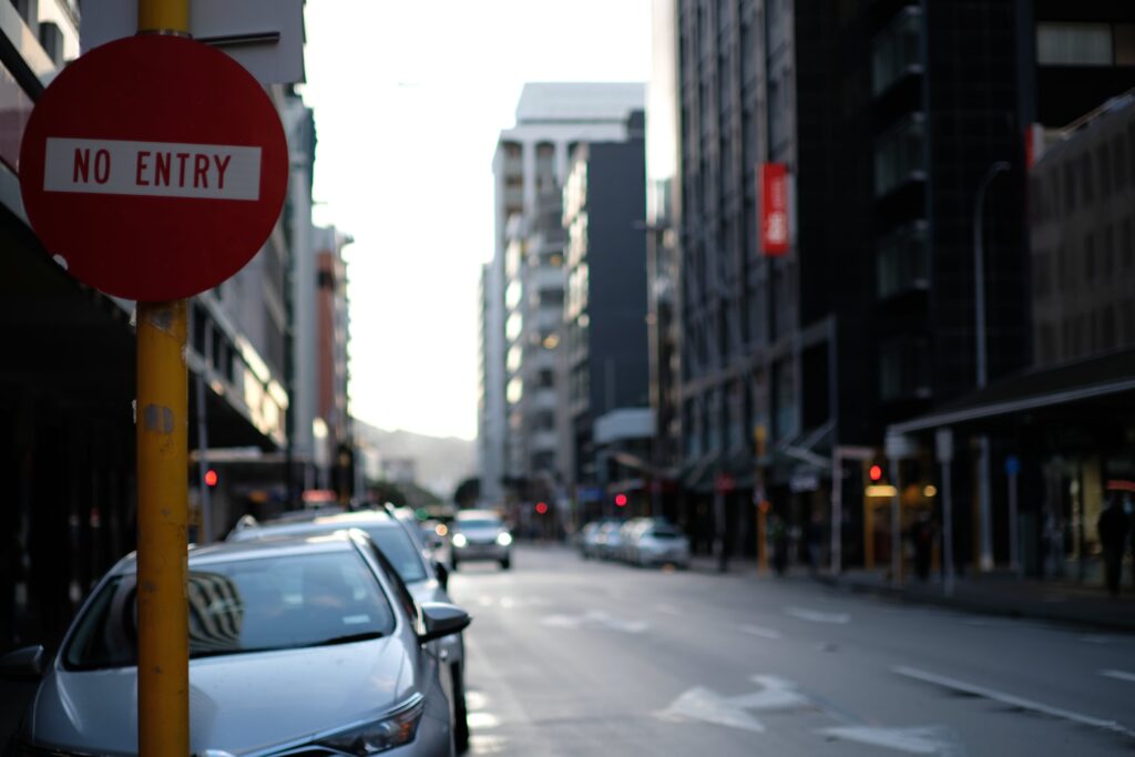 A moody photograph looking down a Wellington street. In the foreground, a No Entry street sign is the only thing in focus. The sky is bright with cloud, the buildings hulking masses of defocused grey.